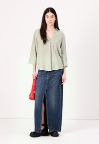 Ljusgrön blus med lång ärm och V-ringning, kombinerad med en blå denim-maxikjol med slits framtill. Svarta klumpiga skor och en röd väska.