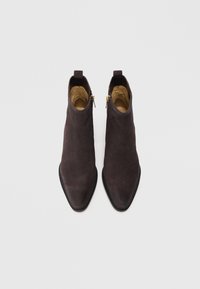 Stivali alla caviglia in suede marrone con punta appuntita, zip laterali e suola in gomma nera. Texture liscia con un design minimalista.