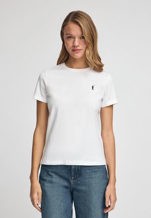 T-shirt bianca in cotone con maniche corte e scollo rotondo. Presenta un piccolo logo grafico nero sul petto. Abbinata a jeans blu.