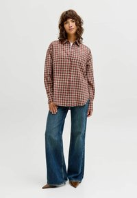 Rdeča in bež karo srajca z gumbi, ohlapen kroj; kombinirana z razširjenimi modrimi jeans hlačami. Obleko dopolnjujejo rjavi čevlji z nazobčanimi konicami.