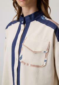 Katoenen shirt met een crèmekleurig lichaam, marineblauwe strepen, een denim kraag en een zak met gestreepte accenten. Knopsluiting met verfijnde stiksels.