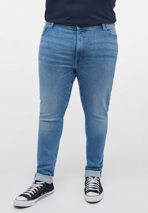 Jeans din denim de un albastru deschis, cu o croială ajustată, decolorare subtilă, cinci buzunare și manșete răsucite. Asortați cu adidași negri cu șireturi albe.