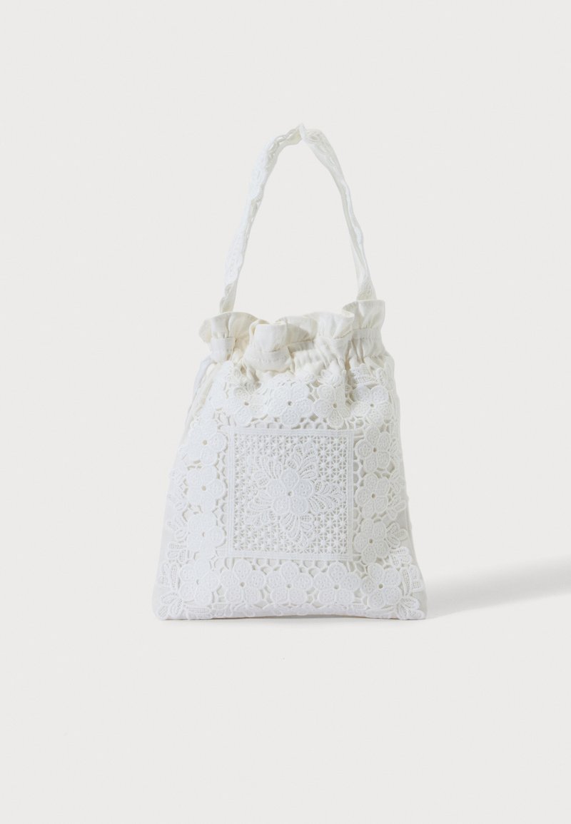 Sac cabas en tissu blanc avec broderie florale en dentelle et anse supérieure froncée, présenté sur un fond clair uni.