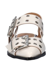 Witte leren schoen met dubbele brede banden met zilveren eyelets en gespen, open zijkanten en een ronde neus op een zwarte zool.