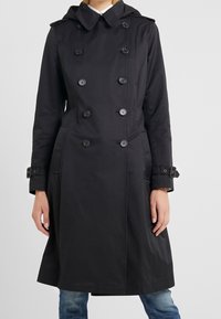 Svart dubbelt knäppt trenchcoat med huva, utrustad med stora knappar, sidofickor och manschettremmar. Slät tyg och stilren design.