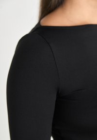 Svart langermet topp med en glatt, tettsittende design og vid halsudringning samt sømløse skulderdetaljer, laget av myk, elastisk stoff.
