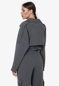 Giacca cropped grigia con ampio colletto, polsini con bottoni e tessuto testurizzato. Il retro presenta un design a strati e due tasche laterali.