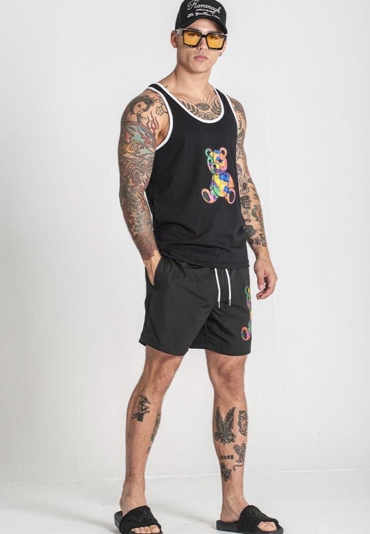 Čierny top bez rukávov s farebnou grafikou medveďa, doplnený čiernymi šortkami so podobným dizajnom medveďa, skombinovaný s šľapkami.