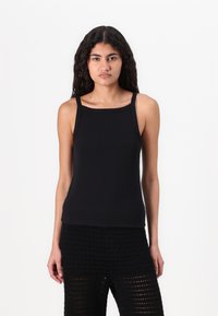 Top nero senza maniche con scollo quadrato e spalline sottili. Realizzato in un tessuto morbido e testurizzato. Abbinato a pantaloni neri con fantasia.