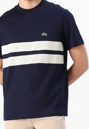 Marineblaues Kurzarmhemd mit zwei horizontalen weißen Mesh-Streifen über der Brust und einem kleinen grünen gestickten Krokodil-Logo.