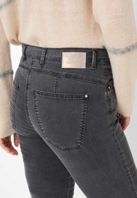 Jeans in denim grigio con vita alta, due tasche posteriori e un'etichetta leggera in rilievo sulla cintura. Tessuto morbido con una leggera elasticità.