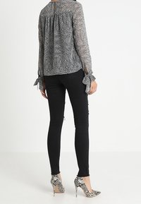 Jeans neri a vita alta abbinati a una blusa trasparente a scacchi in bianco e nero con maniche legate e scollatura a chiave. Tacchi alti in stampa pitone.