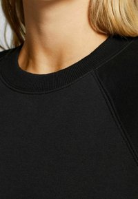 Sudadera negra con cuello acanalado y tela texturizada. El diseño incluye mangas raglán y un acabado suave.