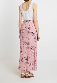 Blumen-Maxi-Rock in Pink mit geraffter Taille, aus leichtem Stoff und zarten Blumenmustern. Kombiniert mit weißen Sandalen.