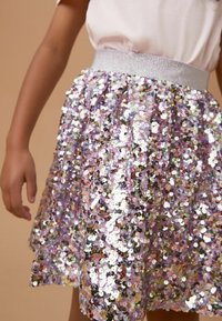 Gonna viola di paillettes con una texture lucida e una cintura elastica argento, che riflette la luce con sfumature variabili di rosa e paillettes argentate.