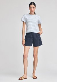 T-shirt a maniche corte a righe in azzurro chiaro e bianco, abbinato a pantaloni cargo blu navy. Sandali con una cintura beige e dettaglio del logo completano l'outfit.