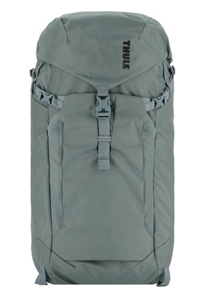 Thule backpack in muted green fabric, featuring adjustable straps, a top buckle, side pockets, and subtle ribbed texture.