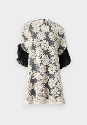 Sukienka w kwiatowy wzór wykonana z przezroczystego materiału, z beżowymi kwiatami na szarym tło w kropki; czarne plisowane krótkie rękawy dodają tekstury.