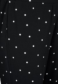 Czarny materiał w białe kropki. Tkanina wydaje się lekka, ma gładką fakturę i charakteryzuje się dopasowanym krojem oraz plisowanymi detalami.