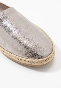 Zapato de espadrille texturizado en color plata metálico con suela de cuerda trenzada beige sobre un fondo blanco.