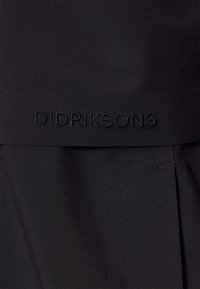 Tissu noir à texture lisse, avec un logo "DIDRIKSONS" en relief. Le design comprend des plis à l'ourlet pour plus de détails.