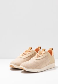 Beige Textilsneaker mit einer strukturierten Oberseite, orangefarbenen Schnürsenkeln und einer gesprenkelten weißen Sohle. Verfügt über eine Lasche an der Ferse für ein einfaches An- und Ausziehen.