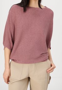 Rento, resoripintainen neule mauvessa, pehmeästä kankaasta valmistettu. Siinä on venepääntie ja leveät hihat, yhdistetty beigenvärisiin housuihin.