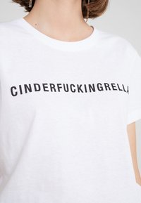 Bílý bavlněný tričko s výrazným černým textem "CINDERFUCKINGRELLA" napsaným přes hruď. Kulatý výstřih.
