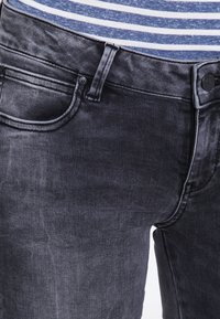 Jeans de mezclilla gris con un ajuste slim, cierre de botón y bolsillos frontales. La tela tiene una textura suave con un sutil efecto de lavado.