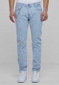 Jeans de mezclilla azul claro, con corte slim, diseño de cinco bolsillos y un acento de cadena plateada sujeto al bolsillo.