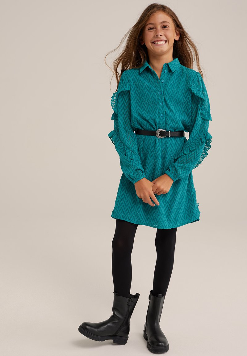 Rochie teal cu un model în zigzag, cu manșete lungi cu volane, închidere cu nasturi în față, talie cu curea, asortată cu colanți negri și cizme scurte.