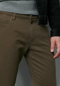 Oliwkowe spodnie o dopasowanym kroju, wykonane z tkaniny typu twill. Posiadają metalowy guzik, kieszenie oraz kontrastowe szycia.