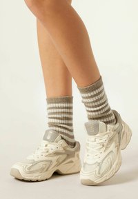 Białe buty sportowe z siateczki i gumowych materiałów, z falistym wzorem, w zestawie z beżowymi i białymi skarpetami w paski wykonanymi z tricot.
