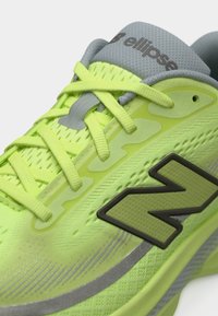 Εγγύς λήψη αθλητικού παπουτσιού νέον πράσινου με γκρι γλώσσα, κίτρινες κορδόνια και σκούρο πράσινο λογότυπο "N" στο πλάι.