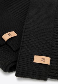 Czarne rękawiczki z prążkowanego dzianego materiału z skórzanymi metkami z logo. Tekstura jest miękka i ciepła, odpowiednia na zimne warunki.