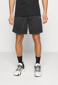 Svarta sportshorts med resårmidja, en slät yta och lätt material, i kombination med mönstrade sneakers i vitt och svart.