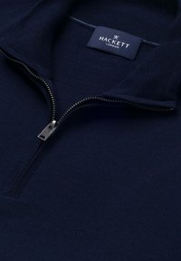 Tmavomodrý pletený sveter s kovovým polovičným zipsom a štítkom Hackett London vo vnútri goliera.