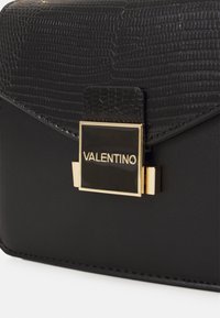 Musta nahkalaukku, jossa on tekstuurilla varustettu krokotyyppinen läppä. Varustettu kultaisella sulkimella, jossa on "Valentino"-brändäys, suorakulmion muotoinen ja tyylikäs muotoilu.