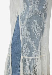 Tissu en dentelle florale blanche avec une fente latérale révélant un tissu en denim bleu en dessous.
