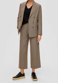 Blazer marron à carreaux et pantalon large assorti, associés à un haut noir texturé et des baskets noires à semelle beige.