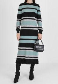 Robe à manches longues rayée en bleu sarcelle, noir et gris. Tissu en maille douce. Associée à un petit sac à bandoulière noir embossé croco et des bottes noires montantes jusqu'au genou.