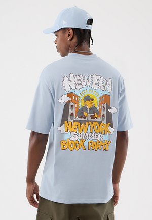 Hombre con camisa azul claro y gorra, espalda de la camisa muestra un dibujo animado de un DJ con altavoces, edificios, sol y texto "New Era New York Summer Block Party."