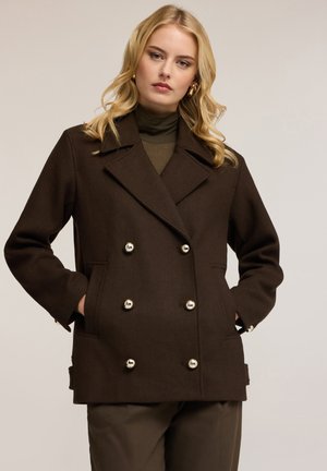 Bruin dubbelzijdig jasje van wol, met glanzende zilveren knopen, brede revers en zijzakken; gedragen over een groene coltrui.