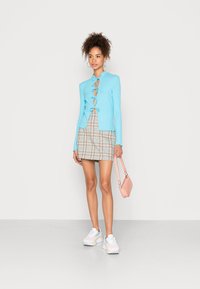 Top de manga longa azul claro canelado com laços à frente, saia mini xadrez, bolsa rosa e ténis brancos com detalhes em tons pastel.