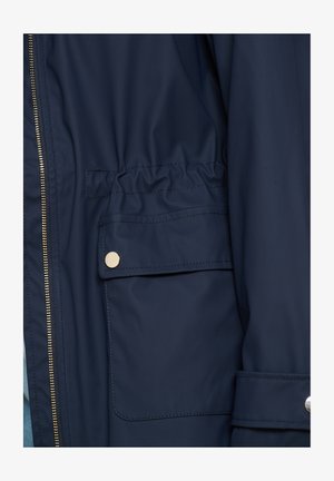 Tumesinine veekindel jope, millel on kuldne tõmblukk, elastne nööriga vöökoht ja küljetasku klõpsuga sulgemisega. Sile tekstuur ja kohandatud lõige.