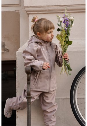 Lysebeige vandtæt jakke med hætte, med et diskret stjernemønster. Kombineret med matchende bukser og katte-temasko, der holder blomster.