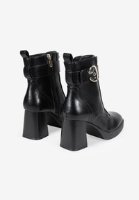 Stivaletti neri in pelle con tacco largo, cerniera laterale e una fibbia decorative in cima. Texture liscia con dettagli cuciti.
