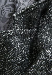 Tissu en mélange de laine dans un motif pied-de-poule noir et blanc, avec une texture douce, doublé d'un gris lisse et présentant des détails de couture visibles.