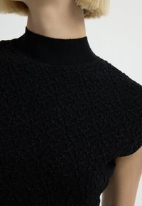 Top nero con texture che presenta un collo alto e un motivo floreale, realizzato in un tessuto leggermente lucido che aggiunge interesse visivo.