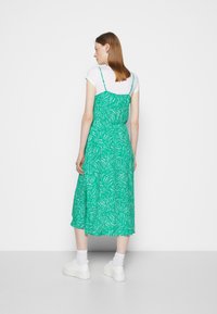 Sundress verde com padrão, alças finas, apresentando um design de folhas e um caimento solto. Combinado com ténis brancos e meias até ao tornozelo.